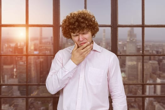Young man with curly hair touching his jaw because of toothache.