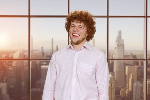 Portrait of a happy young laughing man with curly hair. Checkered window with cityscape view.