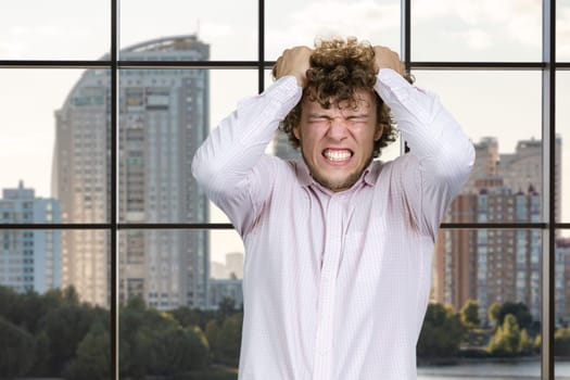 Portrait of a young man with curly hair having nervous breakdown. Indoor window in the background.