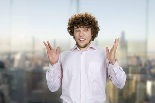 Portrait of surprised shocked young guy with curly hair. Urban cityscape in the background.