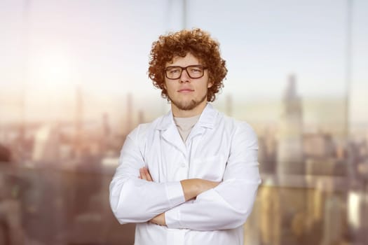 Portrait of a young male cook in white uniform wearing glasses. Blurred cityscape in the background.