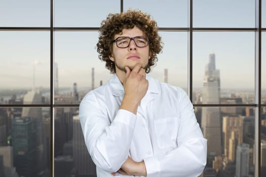 Portrait of a smart thoughtful young man with curly hair. Checkered window with cityscape view in the background.