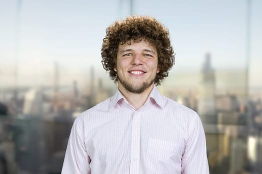 Portrait of a happy young smiling man with curly hair. Cityscape view in the background.