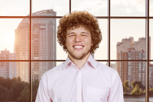 Portrait of a happy young cheerful man with curly hair. Cityscape view in the background.