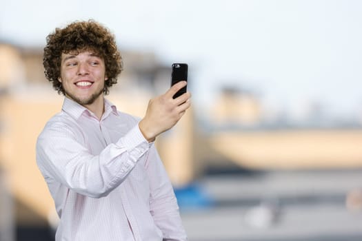 Portrait of a happy smiling young man with curly hair making a selfie. Blurred indoor background.