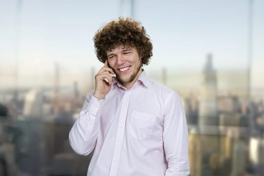 Portrait of a young caucasian man in white shirt talking on the phone. Urban cityscape in the background.