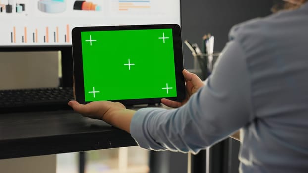 Worker examines greenscreen on tablet in agency coworking space office, looking at chromakey screen with isolated copyspace on mobile gadget. Employee holding chromakey device.