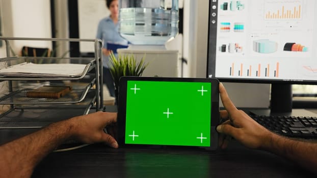 POV of manager uses tablet with greenscreen template, looking at chromakey layout and sitting in coworking space. Young man examining blank mockup copyspace on device display.