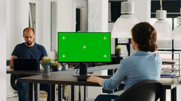 Employee using computer at desk, monitor running greenscreen template in business agency office. Company specialist looking at isolated chromakey display with mockup copyspace, digital network.