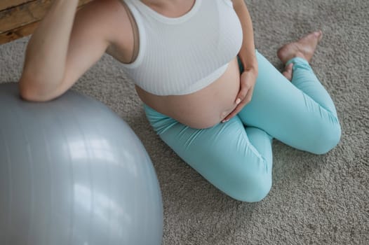 Pregnant woman resting after workout sitting on the floor near the fitness ball