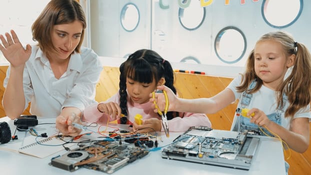 Skilled caucasian teacher teach and explain students about digital electrical tool. Expert girl learn electronic equipment and use to fix motherboard at table with chips and wires placed. Erudition.