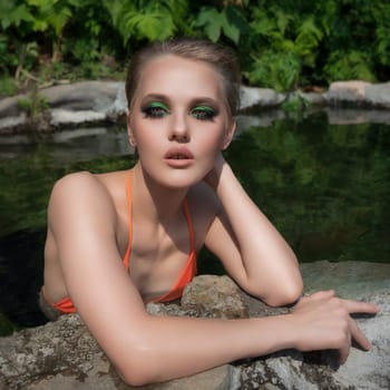 Beautiful woman with short hair and bright makeup wearing an orange colored bikini top. Woman looking at camera while bathing in an outdoor pool with natural geothermal water