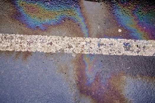 Oil spill on wet asphalt, parking lot with dividing line.