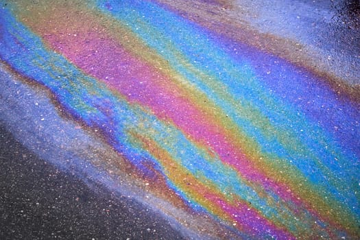 Background texture of an oil spill in the form of a rainbow stain on dark asphalt, parking. Selective focus