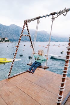 Little girl swings on a rope swing on a pier over the sea. High quality photo