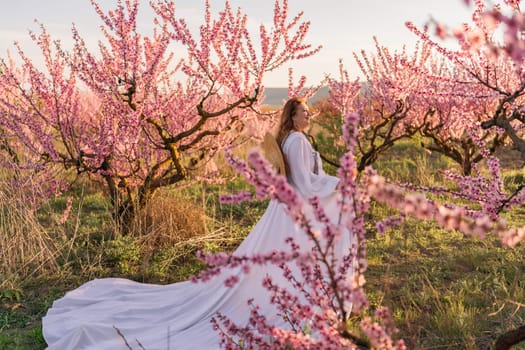 Woman blooming peach orchard. Against the backdrop of a picturesque peach orchard, a woman in a long white dress and hat enjoys a peaceful walk in the park, surrounded by the beauty of nature