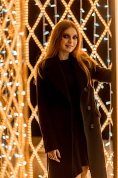 Christmas mood. Woman with long hair in sity decorated for Christmas. She is dressed in a black coat