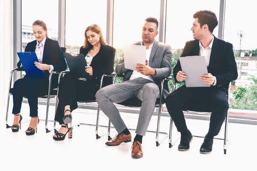 Businesswomen and businessmen holding resume CV folder while waiting on chairs in office for job interview. Corporate business and human resources concept. uds