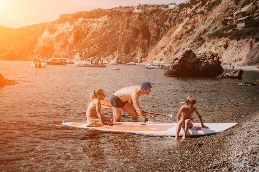 Father and his adorable little son and daughter sitting on stand up board having fun during summer beach vacation