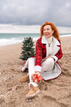 Lady in plaid shirt holding a gift in his hands enjoys beach with Christmas tree. Coastal area. Christmas, New Year holidays concep.