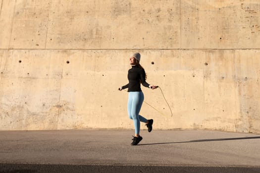 Female athlete doing cardio workout. Young woman in sports clothes jumping the rope. Rope skipping outdoors exercising. Copy space. Active and healthy lifestyle concept.
