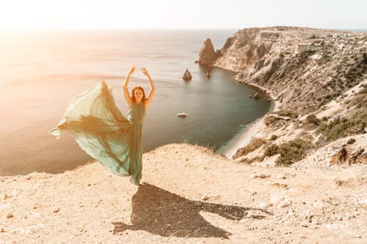 Woman green dress sea. Female dancer posing on a rocky outcrop high above the sea. Girl on the nature on blue sky background. Fashion photo