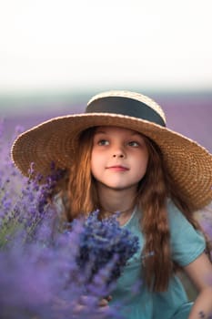 Girl lavender field in a blue dress with flowing hair in a hat stands in a lilac lavender field.