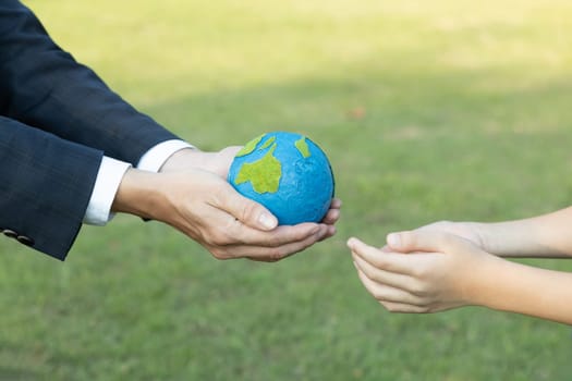 Businessman hand giving Earth globe to little boy as Earth day concept as corporate social responsible to contribute greener environmental protection for sustainable future generation. Gyre