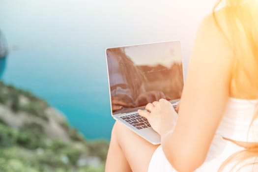 Freelance women sea working on the computer. Good looking middle aged woman typing on a laptop keyboard outdoors with a beautiful sea view. The concept of remote work