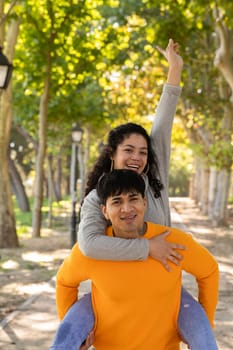 Young couple having fun at a park. Successful woman in piggyback ride with positive mood.