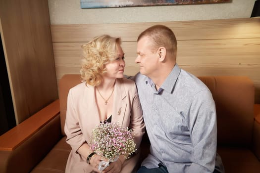 Loving adult couple communicates and embraces privately in the living room or in hotel. Woman is wearing business formal suit and man is wearing jeans and a shirt, indicating a close relationship