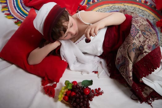 Portrait of Little girl in a stylized Tatar national costume with berries and a brush of grapes on a white background in the studio. Photo shoot of funny young teenager who is not a professional model