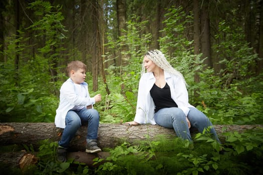 Funny mother with dreadlocks and fat boy happy walking in the forest on a sunny summer day