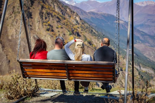 Friends enjoying a conversation on a swing, against the backdrop of majestic mountain scenery