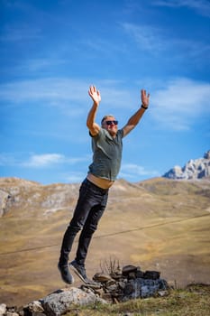 A man happily jumps on the top of a mountain, exhilarating the mesmerizing scenery and his achievement.