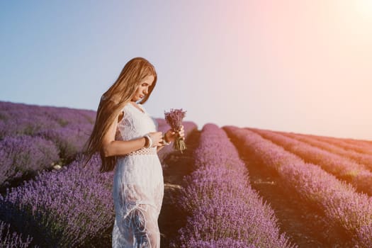 Close up portrait of young beautiful woman in a white dress and a hat is walking in the lavender field and smelling lavender bouquet.