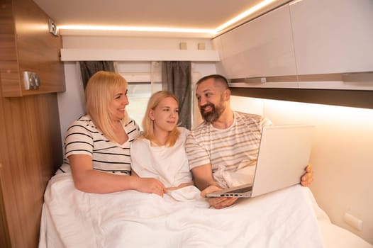 A family of three is watching a movie on a laptop while sitting in the bed of their motorhome.