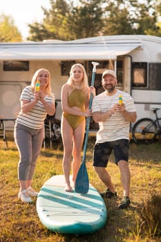 the family is resting next to their mobile home. My daughter is standing with a paddle on a sup board, and her parents pour water on her.