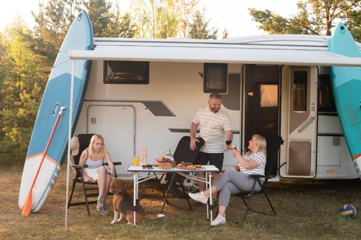 A happy family is resting nearby near their motorhome in the forest.