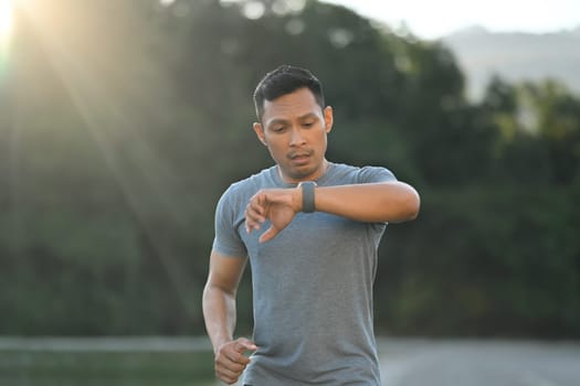 Tired young sporty man check heart rate or monitor healthy body progress during training outdoors.