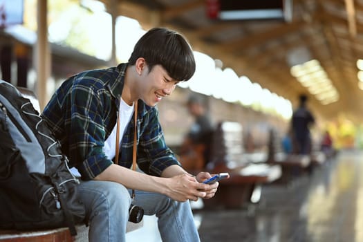 Handsome man backpacker using mobile phone at railway platform. Travel and vacations concept.
