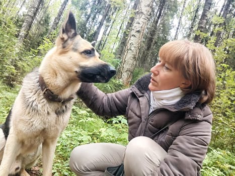 Adult girl with shepherd dog taking selfies in forest. Middle aged woman and big shepherd dog on nature. Friendship, love, communication, fun, hugs