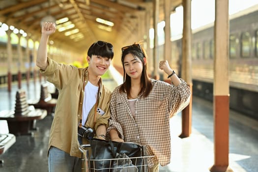 Happy young couple standing in train station, excited about their vacation. Travel and lifestyle concept