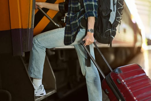 Cropped shot male traveler with suitcase getting on the train. Travel and vacations concept.