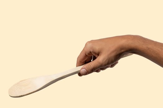 Male hand holding wooden spoon on light beige background. High quality photo