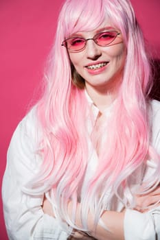 Close-up portrait of a young woman with braces in a pink wig and sunglasses on a pink background. Vertical photo