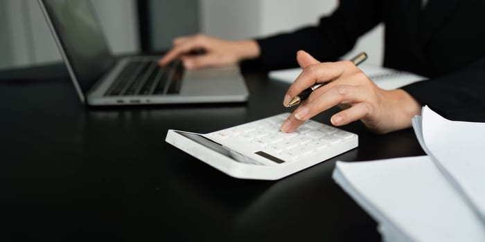 Businesswoman using a calculator to calculate numbers on a company's financial documents, she is analyzing historical financial data to plan how to grow the company. Financial concept.