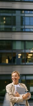 Woman freelancer standing with laptop and coffee cup on modern building background during break time