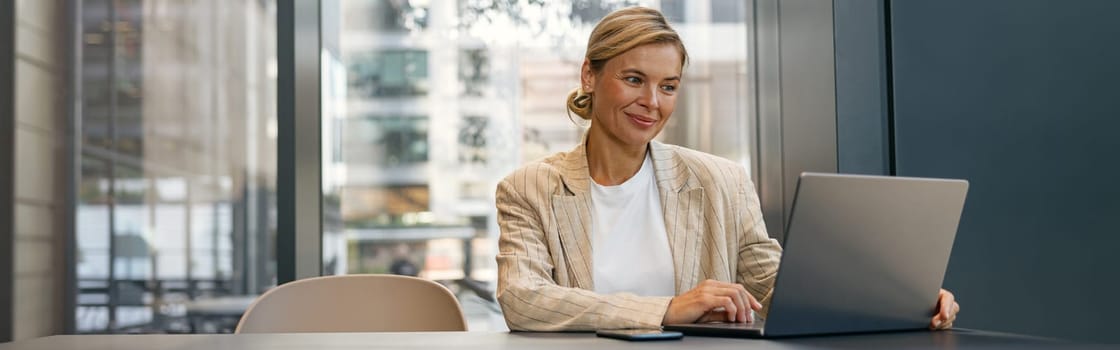 Stylish business woman working on laptop sitting the desk on office background