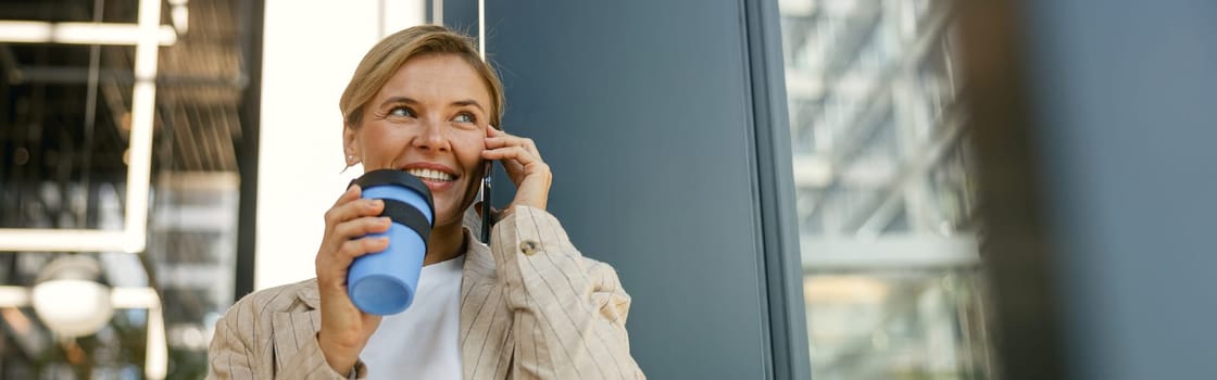 Smiling stylish business woman talking phone with client while standing near office building